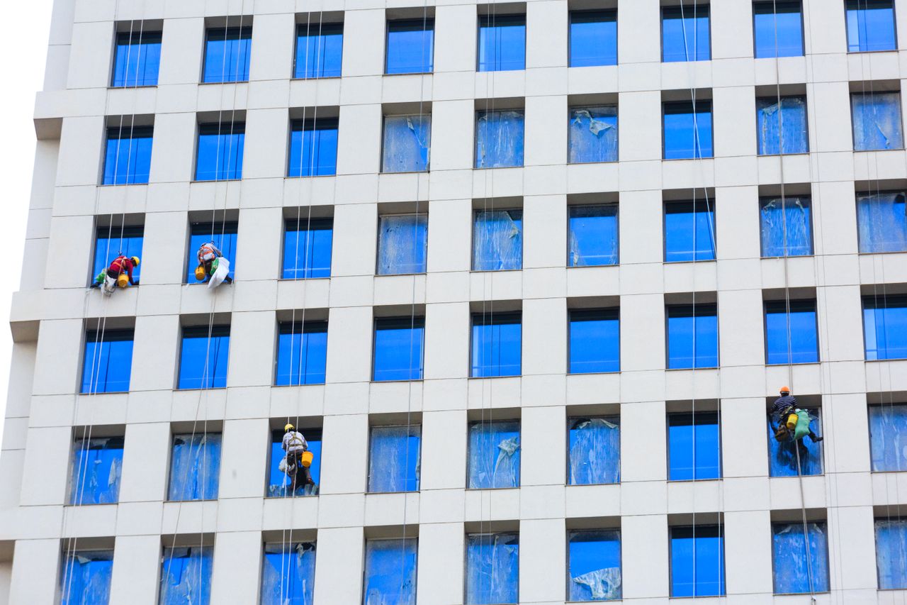 services-01 Professional workers clean skyscraper windows using ropes in urban setting.